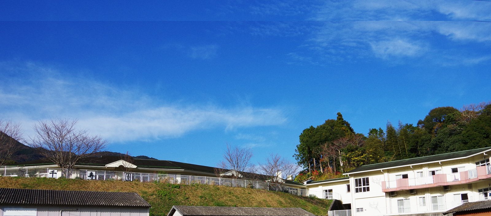 介護施設の建物外観。丘陵地に立つ複数棟の施設と周辺の自然風景